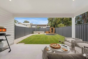 A backyard patio with a dining table, chairs, and a pizza. - The White House - Beach Steps & Mountain Views (East Corrimal)