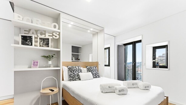 A modern hotel room with a bed, a chair, a mirror, and a view of the city. - Guestready - Old City Design Apartments (Porto)