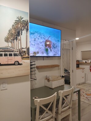A living room with a television displaying a sea turtle, a dining table with chairs, a kitchen area, and a view of a pink van outside. - Perfect studio: solo, couple or family+kids.
Sleeps 4 adults comfortably + crib (El Cajon)