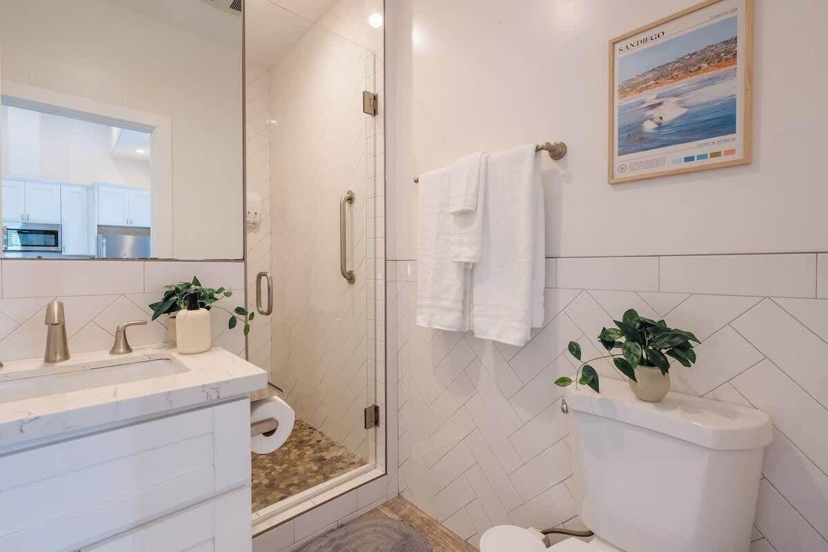 A modern bathroom with a glass shower enclosure, a white sink with a marble countertop, and a toilet with a white tank.