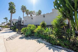 A gated entrance with a palm tree-lined pathway leading to a building with a white facade and a metal gate.