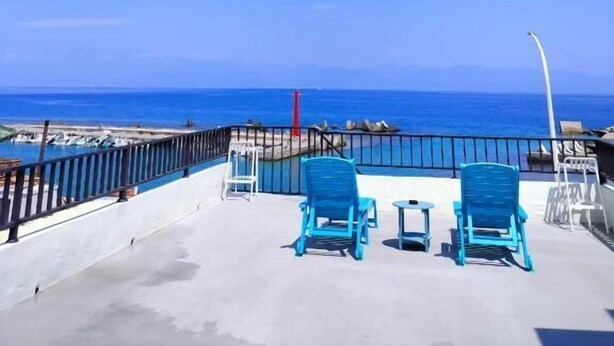 Un balcón con dos sillas azules y una mesita, con vistas a una playa y al mar.