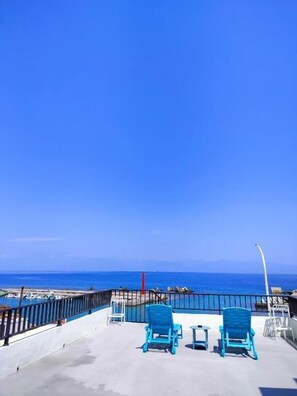Un balcón con dos sillas azules y una mesita, con vistas a una playa y al mar.