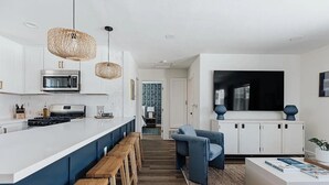 Una cocina moderna con una isla central, taburetes de bar y una zona de estar con un sofá azul.