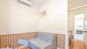 A compact room with a bed, a small table, and an air conditioning unit. - Guestready - Urban Garden Apartments (Lisbon)