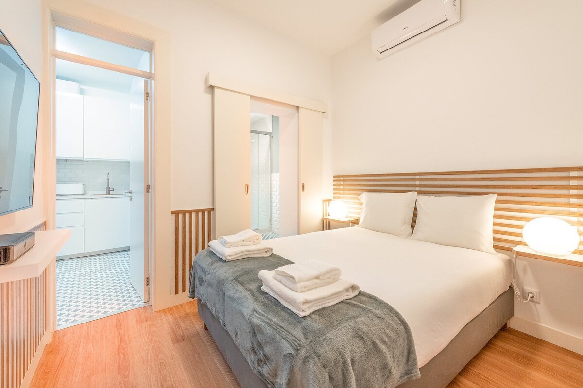 Une chambre d’hôtel avec un lit, des lampes de chevet, une télévision et une salle de bain avec douche, donnant sur l’extérieur.