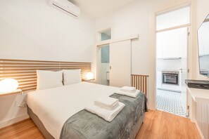 Een moderne hotelkamer met een groot bed, nachtlampen, een kitchenette en een balkon met betegelde vloer.