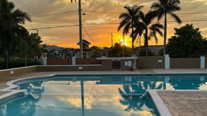 A swimming pool with a stone deck, surrounded by palm trees and houses, during sunset. - RHE Drax Hall Ocho Rios Gated/Pool/Gym (Saint Ann's Bay)