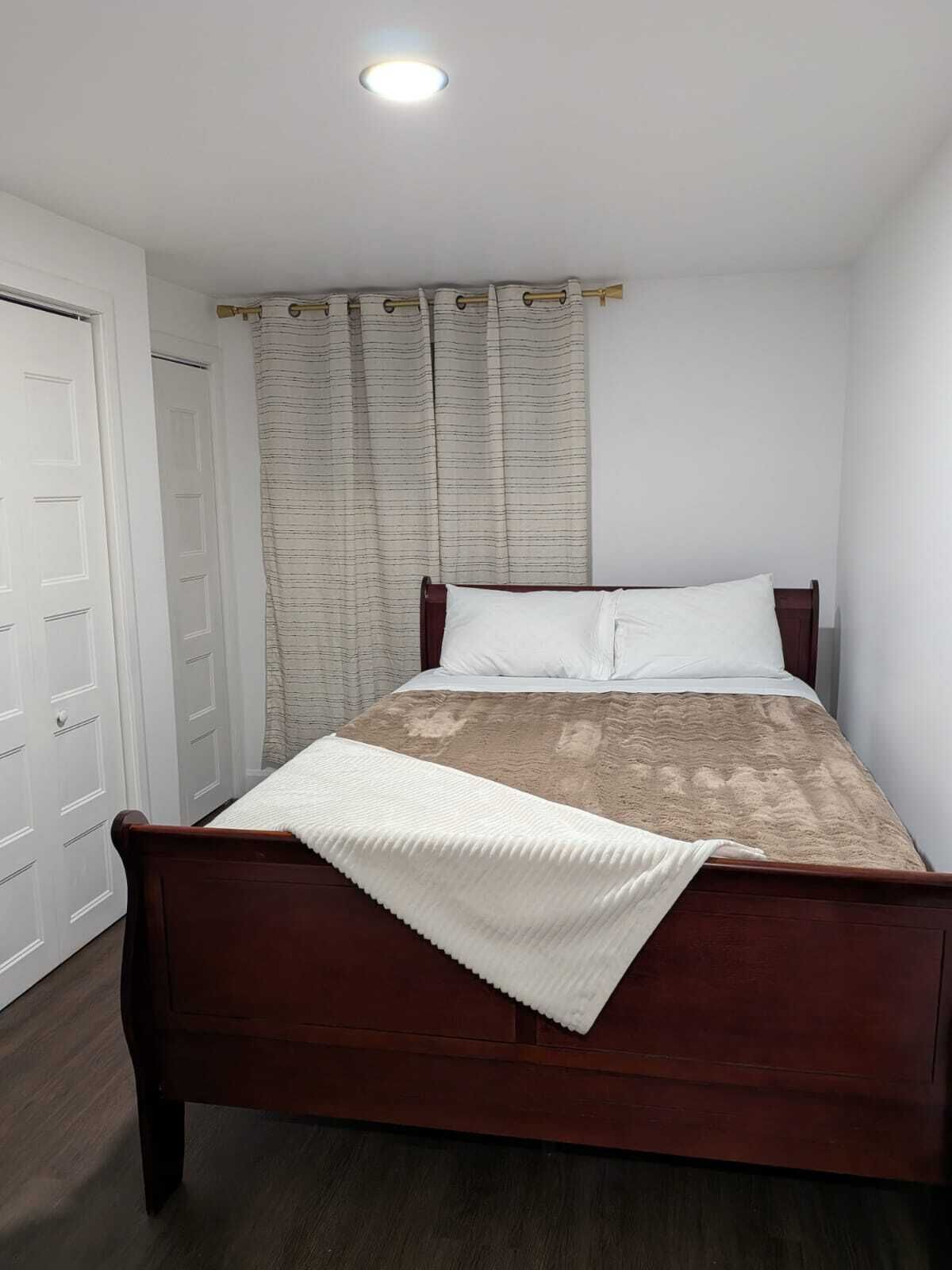 Een enkel bed met houten frame, wit beddengoed en een beige deken.