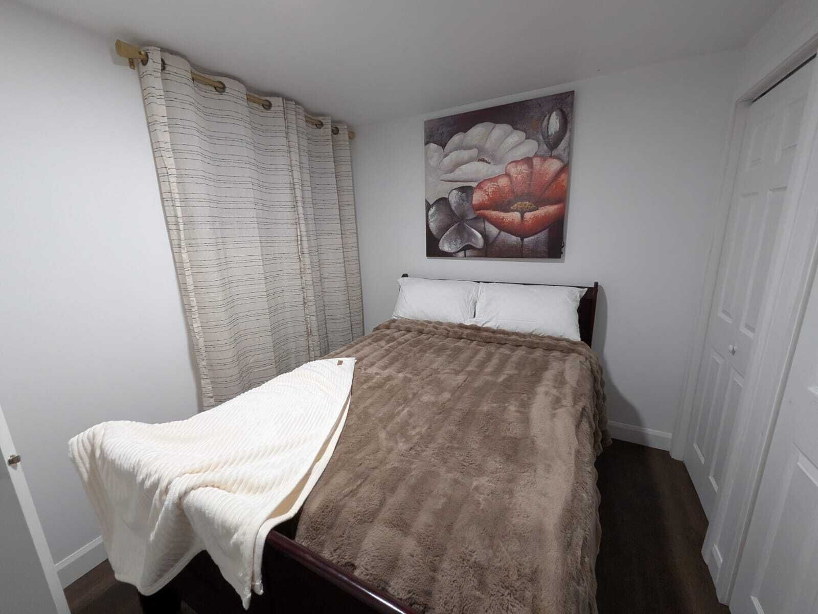 A bedroom with a bed, a white curtain, a painting of flowers, and a door.