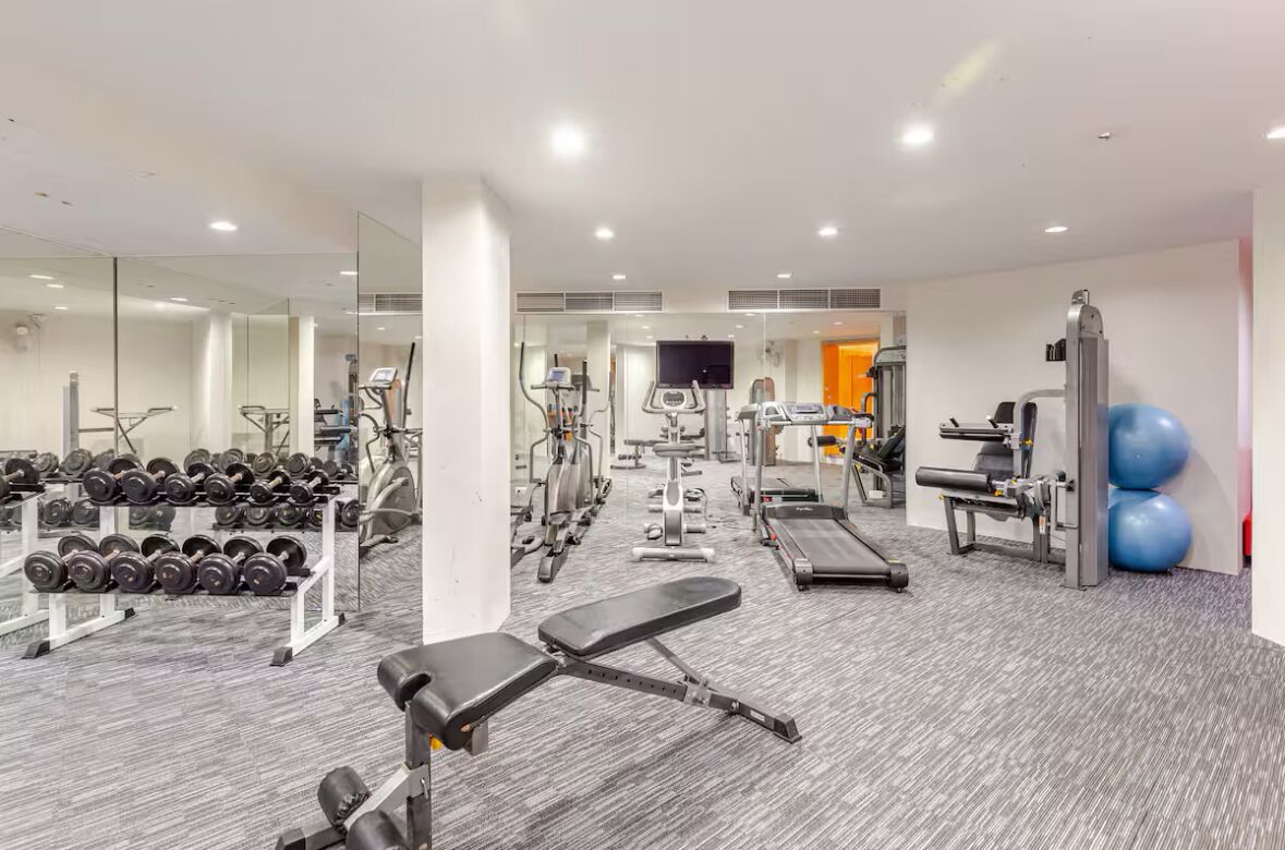 A modern gym with various exercise equipment, a bench, and a mirrored wall.