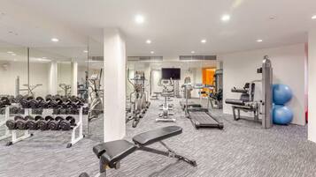 A modern gym with various exercise equipment, a bench, and a mirrored wall.