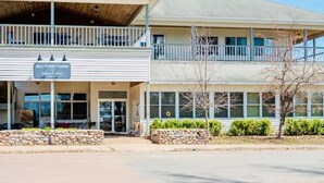 A two-story building with a balcony, a sign reading 'Bell Street Tavern,' and a stone wall in front. - T West Lodging at Bell Street (La Pointe)