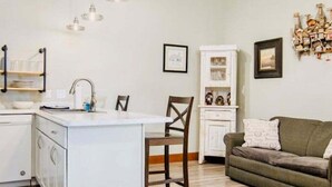 A kitchen with a central island, a dining area with a chair, a sofa, and a cabinet with decorative items. - T West Lodging at Bell Street (La Pointe)