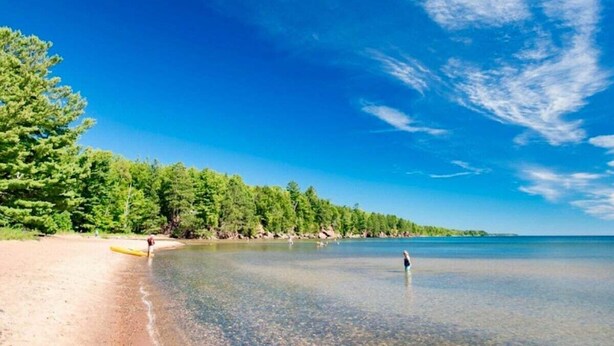A beach with clear water, a sandy shore, and a forested area in the background. - T West Lodging at Bell Street (La Pointe)