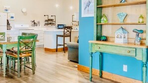 A room with a dining table, chairs, a kitchen area, a ceiling fan, and a shelf with decorative items. - T West Lodging at Bell Street (La Pointe)