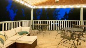 A covered outdoor seating area with a wooden ceiling, white railing, and a view of trees at night. - T West Lodging at Bell Street (La Pointe)