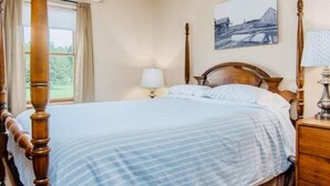 Una camera da letto con un letto a baldacchino, un comodino con una lampada, una finestra con tende e un quadro appeso al muro.