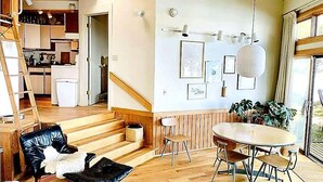 Un vaste espace de vie agrémenté d’un escalier en bois, d’une table à manger avec des chaises, et d’une cuisine en arrière-plan.