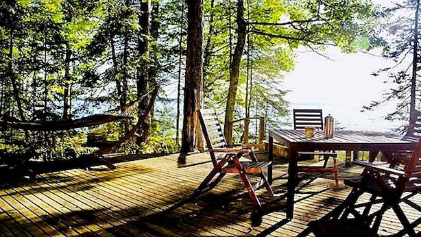 Une terrasse en bois avec une table et des chaises, entourée d’arbres.