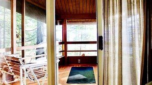 L’intérieur d’une cabane en bois, avec une table à manger, des chaises, une fenêtre et une vue sur la forêt.