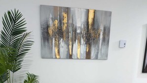 Ein graues Ecksofa mit weißer Decke, ein großes abstraktes Gemälde an der Wand und eine Topfpflanze links.