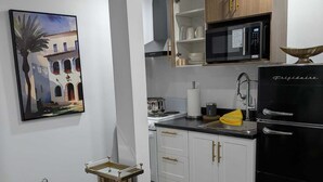 Eine moderne Küche mit weißen Schränken, einem schwarzen Kühlschrank, einer Mikrowelle und einem Gemälde eines Gebäudes an der Wand.