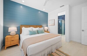 A bedroom with a bed, nightstands, a blue wall, a door leading to a bathroom, and a small rug. - Luxury Lido Escape w/ Pool, Slide, Spa & Rooftop! (Sarasota)