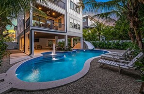 Una casa de dos pisos con piscina, muebles de exterior y un tobogán.