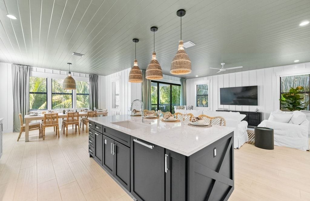A modern kitchen with a large island, pendant lighting, and a dining area with wooden chairs.