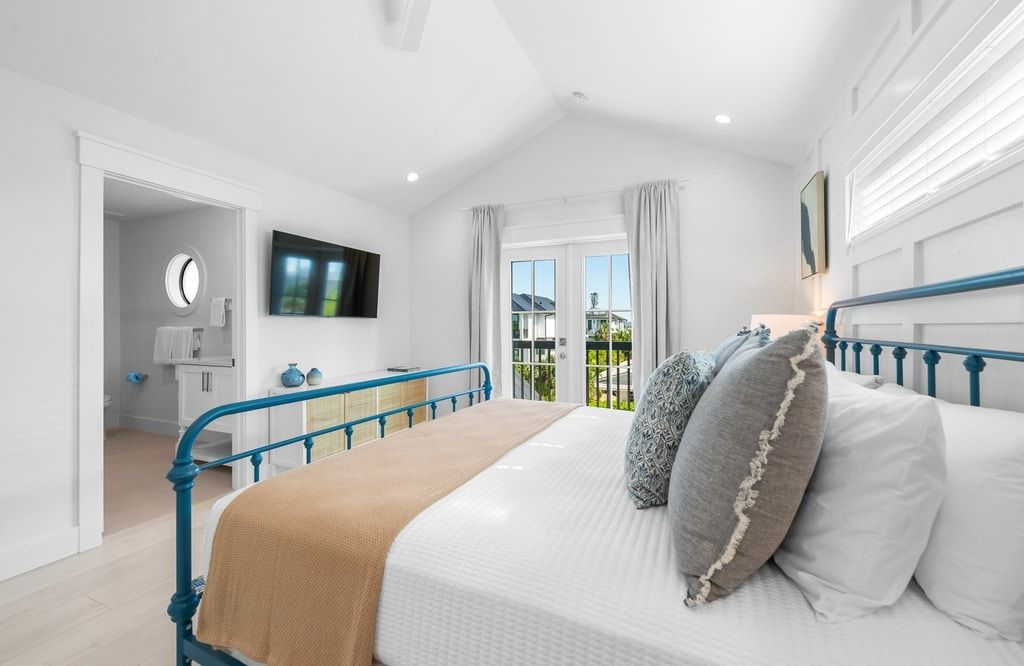 Een slaapkamer met een bed, een televisie, een raam met gordijnen en uitzicht op het omliggende landschap.
