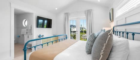 Een slaapkamer met een bed, een televisie, een raam met gordijnen en uitzicht op het omliggende landschap.