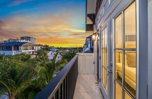 A balcony with a view of a sunset over a residential area, including houses and palm trees. - Luxury Lido Escape w/ Pool, Slide, Spa & Rooftop! (Sarasota)