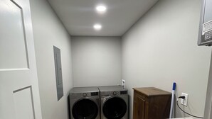 Une buanderie équipée de deux machines à laver à chargement frontal, d’un meuble en bois et d’un plan de travail blanc.