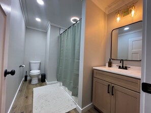 Een badkamer met toilet, douchegordijn, wastafel, spiegel en houten kasten.