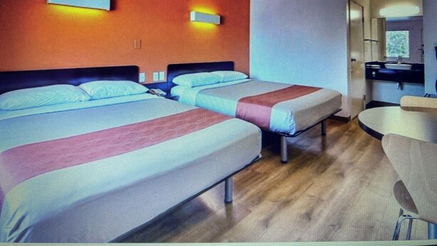 A hotel room with two beds, a desk, and a bathroom.