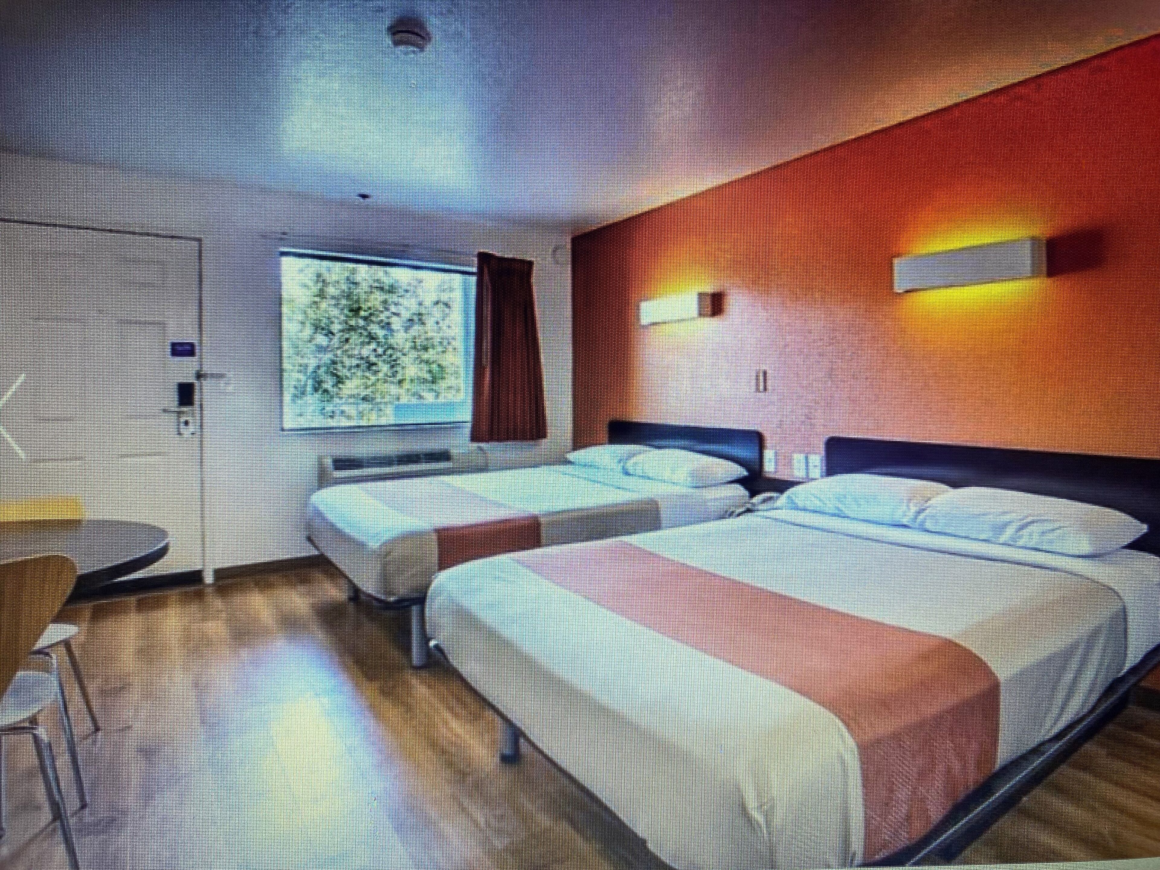 Ein Hotelzimmer mit zwei Betten, einem kleinen Tisch und einem Fenster mit Vorhängen.
