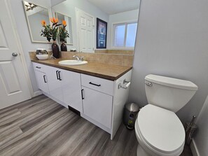 A modern bathroom with a white toilet, a sink with a beige countertop, and white cabinets.