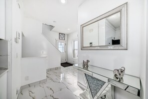 A hallway with a glass console table, a large mirror, and a marble floor.