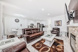 A modern living room with a brown leather sofa, a glass coffee table, and a fireplace.