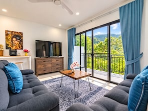 A modern living room with a flat-screen TV, a wooden cabinet, and a balcony with a view of greenery. - Brand New Private Pool Villa Chalong Phuket Mountain View (Chalong)