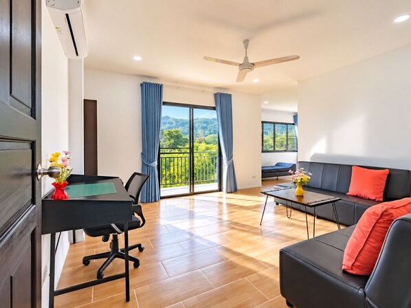 Un salon moderne comprenant un canapé, une table à manger avec des chaises, un balcon donnant sur un espace verdoyant et un ventilateur de plafond.