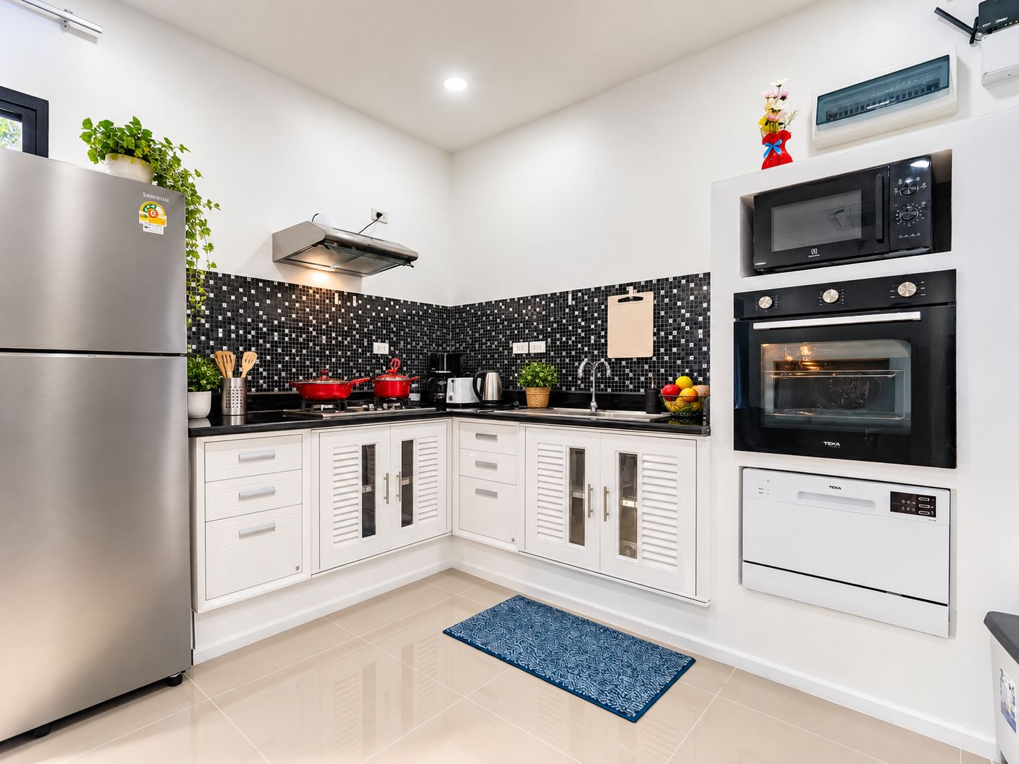 Een moderne keuken met een koelkast van roestvrij staal, een magnetron, een oven en een zwart betegelde spatwand.
