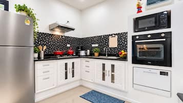 A modern kitchen with a stainless steel refrigerator, a microwave, an oven, and a black tiled backsplash.