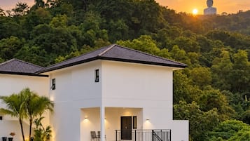 A modern two-story building with a flat roof, a balcony, and a view of a large Buddha statue in the background.