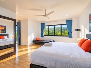 Une chambre d’hôtel moderne dotée d’un grand lit, d’un ventilateur de plafond, d’une fenêtre avec des rideaux et offrant une vue sur la verdure environnante.