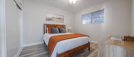 A bedroom with a wooden bed, a ceiling fan, a window with blinds, and a small table with a basket.