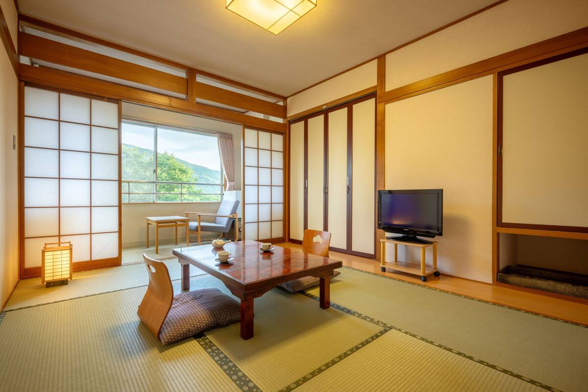 A traditional Japanese room with tatami flooring, a low table, a television, and sliding doors.