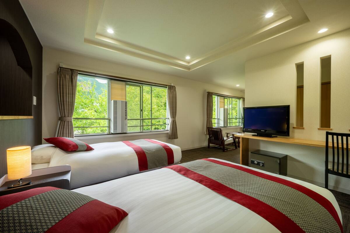 A hotel room with two beds, a TV, a desk, and a chair.