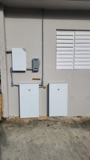 Ein Hauswirtschaftsraum mit zwei weißen Stromverteilern, einem Verteilerkasten und einem Fenster mit horizontalen Rollläden.